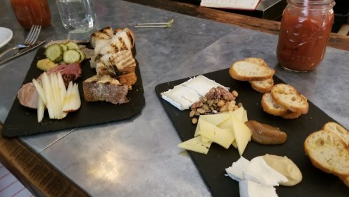 A charcuterie board with assorted cheeses, meats, pickles, bread, and nuts on slate platters.