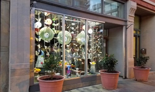 A storefront window displays decorative items and plants in large pots, creating a vibrant and inviting scene.