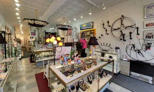A colorful gift shop interior featuring displays of jewelry, art, and decorative items, with bright lighting and unique decor.