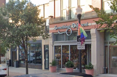 Storefront of "Something Different" with colorful flags and potted plants on a city street.