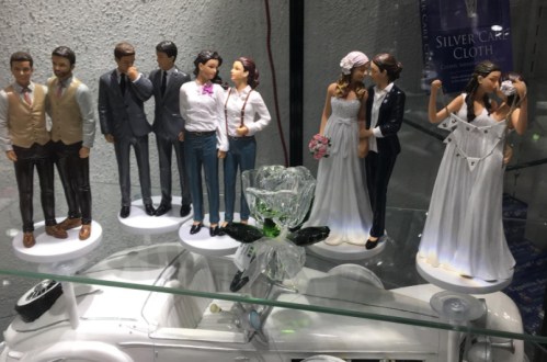A display of wedding cake toppers featuring various couples and groomsmen figurines, with a decorative glass rose.