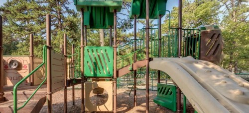 Colorful playground equipment with slides and climbing structures surrounded by trees.