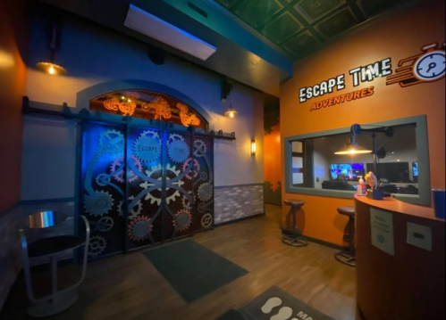 Interior of an escape room venue featuring a gear-themed door, colorful lighting, and a welcoming reception area.