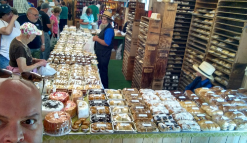 A bustling market scene with a variety of baked goods on display, and people browsing the stalls.