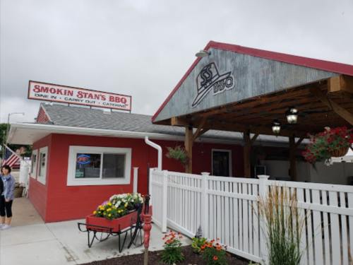 Exterior of Smokin' Stan's BBQ, featuring a red building, covered patio, and flower planters, under a cloudy sky.