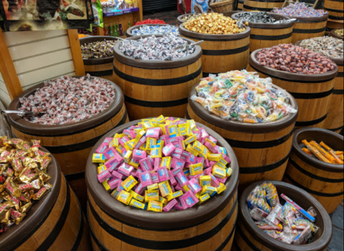 Colorful barrels filled with various candies, including wrapped chocolates and gummies, in a vibrant candy shop.