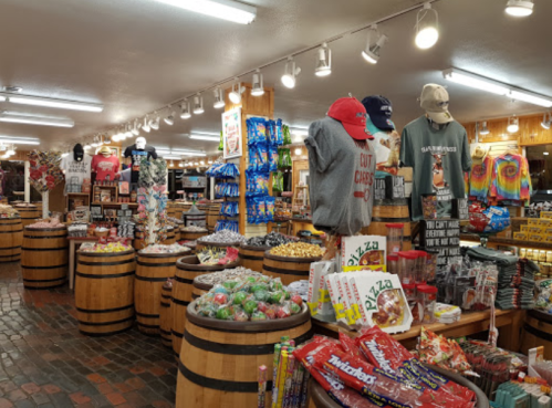 A colorful store interior filled with snacks, souvenirs, and merchandise displayed on barrels and shelves.