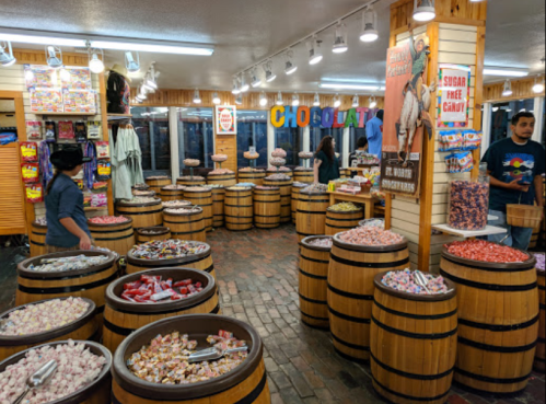 A colorful candy shop with barrels filled with various candies and a few customers browsing the selection.