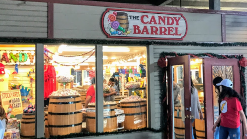 A colorful candy shop named "The Candy Barrel" with barrels of sweets and festive decorations.