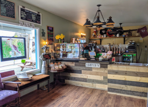 Cozy café interior with a wooden counter, coffee display, and colorful decor, featuring a window and seating area.