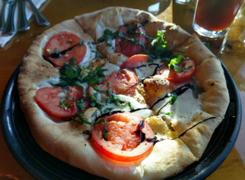 A freshly baked pizza topped with tomatoes, herbs, and drizzled with balsamic glaze on a black plate.