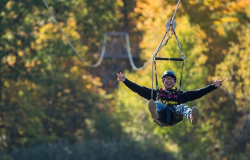 A person joyfully zip-lining through a colorful autumn forest, arms outstretched and smiling.