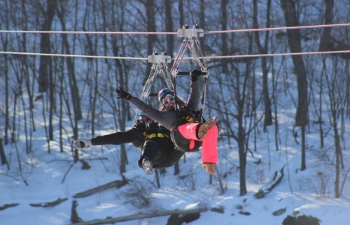 Two people ziplining through a snowy forest, smiling and enjoying the thrill of the ride.
