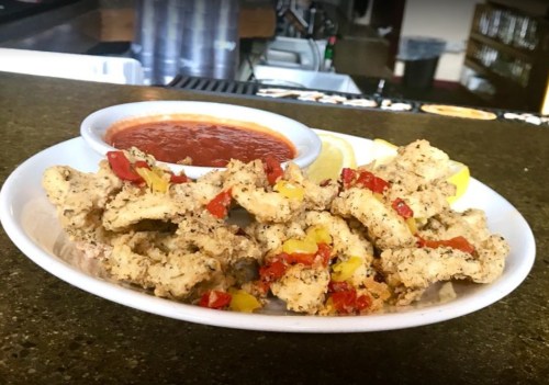 A plate of crispy fried chicken strips topped with bell peppers, served with a side of marinara sauce and lemon wedges.