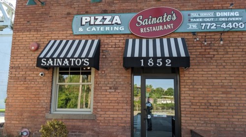 Exterior of Sainato's Restaurant, featuring a brick facade, striped awnings, and signage for pizza and catering services.