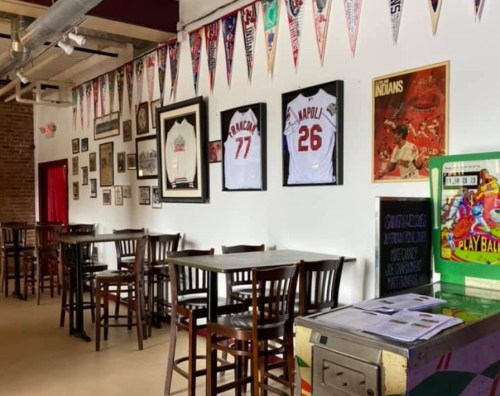 A sports-themed interior with jerseys, framed photos, and banners on the walls, along with wooden tables and chairs.