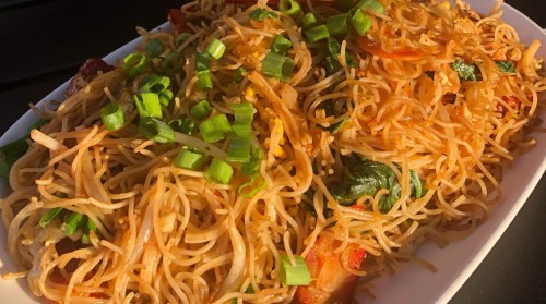 A close-up of a plate of stir-fried noodles topped with green onions and mixed vegetables.