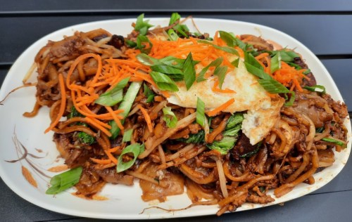 A plate of stir-fried noodles topped with vegetables, an egg, and garnished with green onions and carrots.