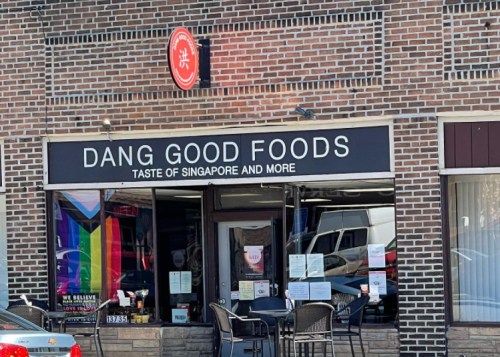 Exterior of a restaurant named "Dang Good Foods," featuring a sign and colorful flags, promoting Singaporean cuisine.