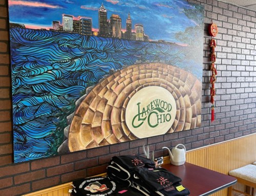 A mural of a city skyline over water, with Lakewood Chio logo, and T-shirts displayed on a table in a cozy restaurant.