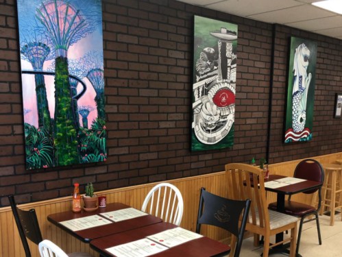 A cozy restaurant interior featuring colorful wall art and wooden tables and chairs. Menus are placed on the tables.