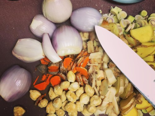 Chopped vegetables including shallots, ginger, and carrots, with a knife resting on a cutting board.