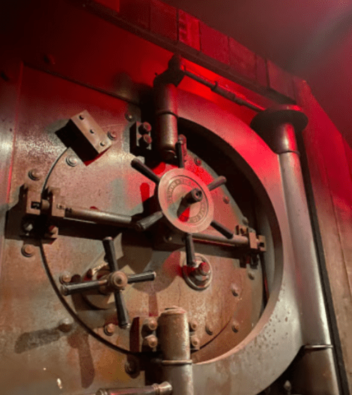 Close-up of a large, metallic vault door with a circular locking mechanism, illuminated by red light.