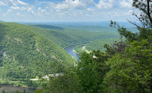 A scenic view of a winding river surrounded by lush green hills under a partly cloudy sky.