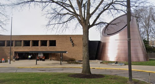 A modern building with a large copper structure beside it, surrounded by trees and a grassy area.