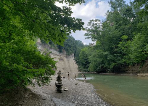 A serene river scene with people wading, surrounded by lush greenery and steep rock formations.