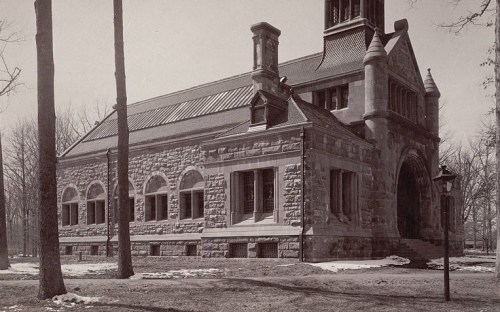 Historic stone building with a tower, surrounded by trees and a lamp post, in a winter landscape.