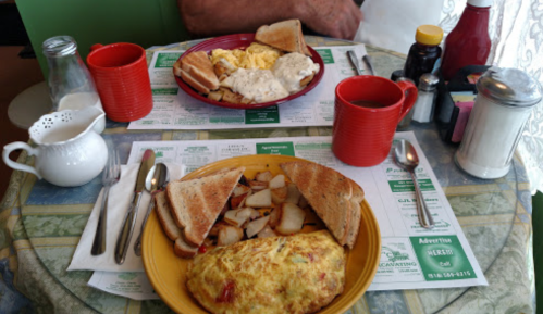 A breakfast table with an omelet, toast, potatoes, scrambled eggs, biscuits, and coffee in red mugs.