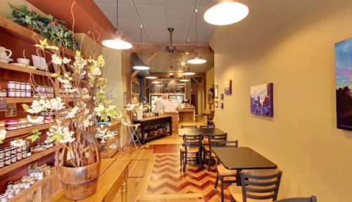 Cozy café interior with wooden shelves, tables, and artwork, featuring a warm color palette and inviting atmosphere.