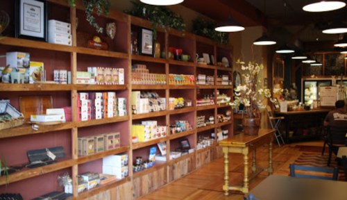 A cozy café interior featuring wooden shelves filled with various packaged goods and decorative plants.