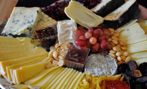 A colorful cheese platter featuring various cheeses, grapes, nuts, and spreads arranged artfully.