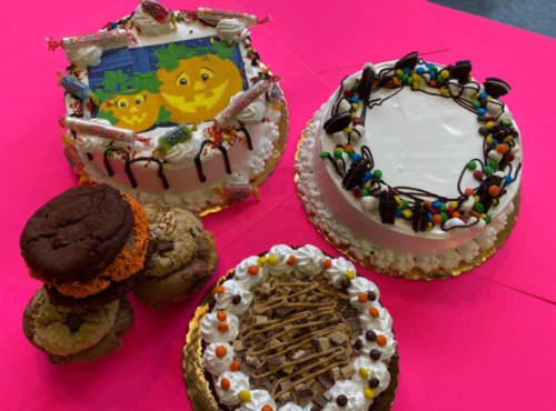 A colorful display of decorated cakes and cookies on a bright pink background, featuring Halloween themes and candy.