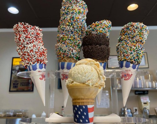 A display of ice cream cones topped with colorful sprinkles, featuring a patriotic-themed cone in the foreground.
