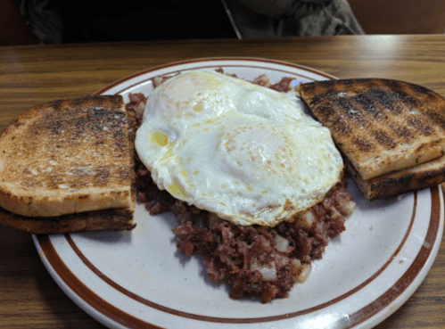 A plate with two fried eggs on a bed of corned beef hash, flanked by two slices of toasted bread.