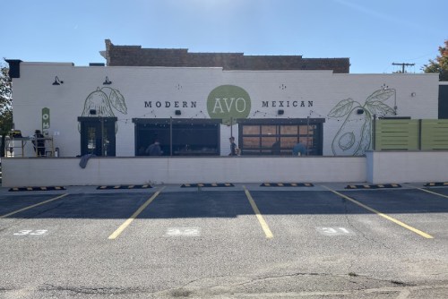 Exterior of a restaurant named "Avo Modern Mexican," featuring avocado-themed murals and a parking lot.