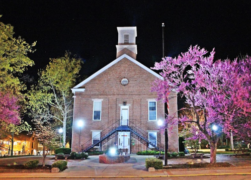 Historic brick building at night, surrounded by blooming pink trees and illuminated by streetlights.