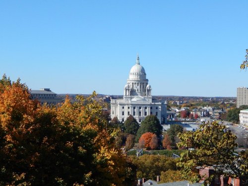 A view of a grand capitol building surrounded by autumn trees under a clear blue sky.