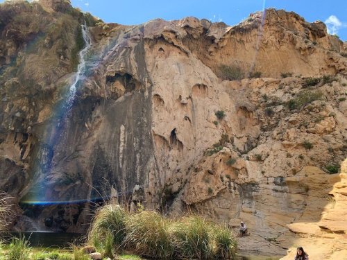 A scenic waterfall cascading down a rocky cliff, surrounded by greenery and a clear blue sky.