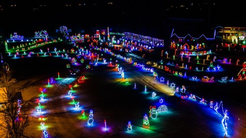 Aerial view of a festive display featuring colorful holiday lights in various shapes and designs across a dark landscape.