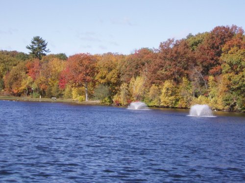 A serene lake surrounded by vibrant autumn foliage and two fountains spraying water.