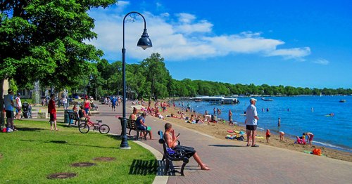 A sunny beach scene with people swimming, sunbathing, and enjoying the outdoors along a sandy shore.