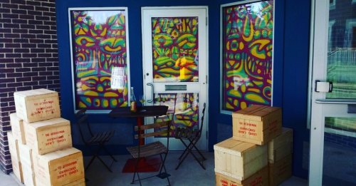 Colorful stained glass windows adorn a porch with stacked wooden boxes and a small table and chairs.