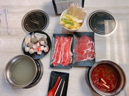 A table set for hot pot with raw meats, seafood, vegetables, and broth, ready for cooking.