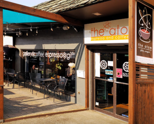 Exterior view of a coffee shop with outdoor seating, featuring a sign that reads "the atom espresso and coffee."