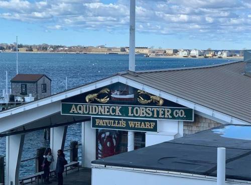 Sign for Aquidneck Lobster Co. at Fatuli's Wharf, with a view of the water and clouds in the background.