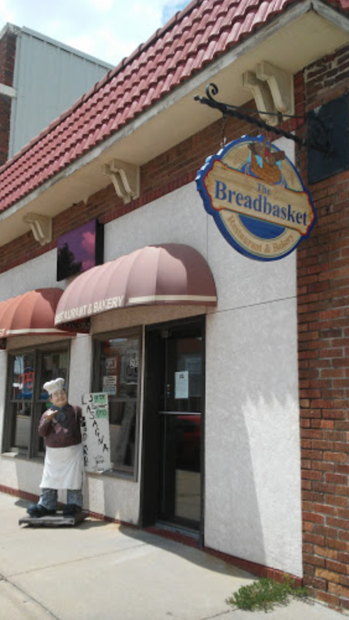 Exterior of The Breadbasket restaurant and bakery, featuring a sign and a statue of a chef outside the entrance.